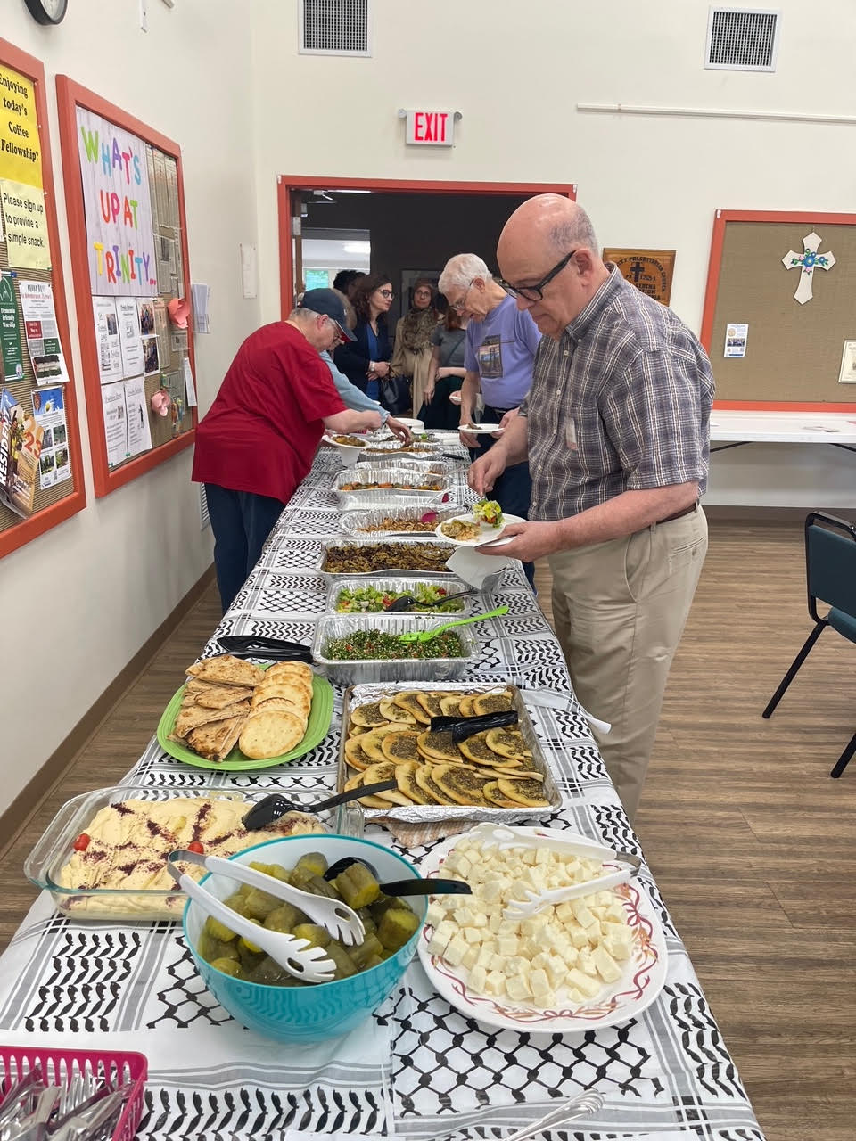 Pictured here is the long table that you'll regularly see at our Trinity Presbyterian gatherings full of food! Also pictured are members making plates for the meal.